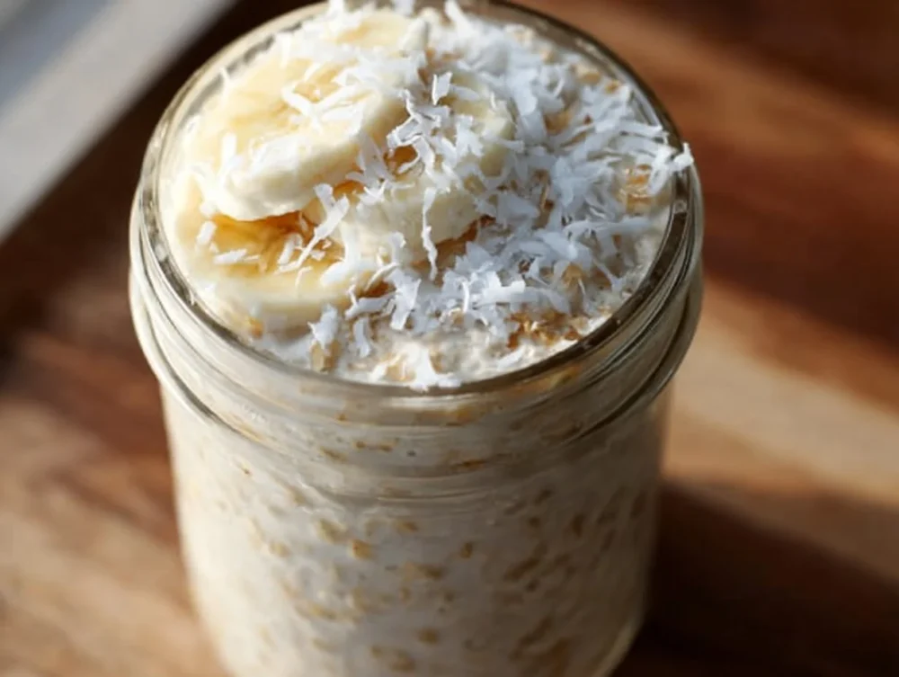 A bowl of banana and coconut overnight oats topped with fruits and nuts.