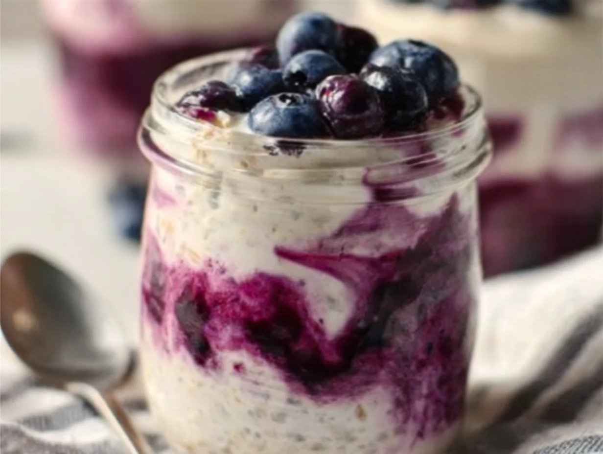 Delicious blueberry cheesecake overnight oats topped with fresh blueberries and a creamy layer.